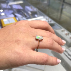 May include: A gold ring with a white opal gemstone. The opal is a rectangular shape with a slight curve. The ring is on a person's finger.