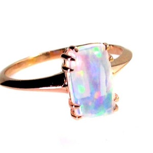May include: A rose gold ring with a large, rectangular, iridescent opal gemstone.