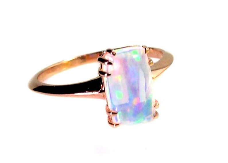 May include: A rose gold ring with a large, rectangular, iridescent opal gemstone.