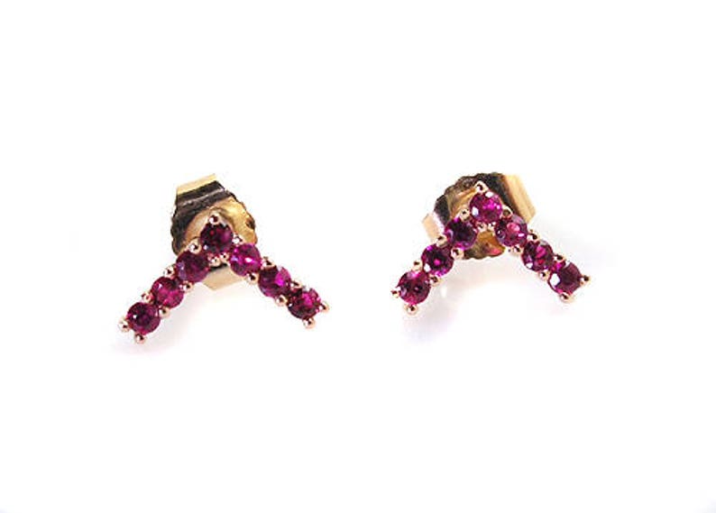 May include: A pair of gold earrings with a V-shaped design set with small, bright pink gemstones.
