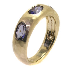 May include: A gold band ring with three purple gemstones set into the band. The ring has a hammered texture.