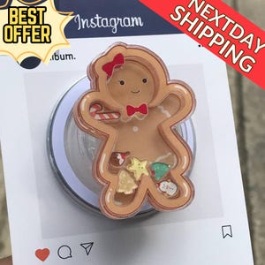Könnte beinhalten: Ein Handyhalter in Form eines Lebkuchenmannes mit roter Schleife und Fliege. Der Halter enthält kleine weihnachtliche Dekorationen. Das Bild hat den Text "Best Offer" und "Next Day Shipping".