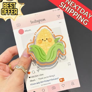 Puede incluir: Una tarjeta rosa con temática de Instagram con un personaje de dibujos animados de maíz con una cara sonriente. La tarjeta incluye el logotipo de Instagram, un icono de corazón y el texto "Album. Thank you for liking it." La tarjeta también tiene el texto "BEST OFFER" y "NEXTDAY SHIPPING".
