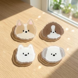 May include: Four acrylic charms featuring stylised dog faces. The top left is a tan and white dog, the top right is a brown and white dog, the bottom left is a white dog, and the bottom right is a white dog with grey ears. Each charm has a clear border.