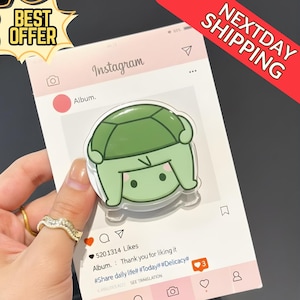 May include: A clear acrylic turtle-shaped sticker with a green shell and light green body, held against a pink Instagram-themed background. The background includes the Instagram logo and a comment section. The words "BEST OFFER" and "NEXTDAY SHIPPING" are also visible.