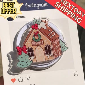 Op de afbeelding: Een gingerbread house-vormige pin met het woord "LIBRARY" op de voorkant. De pin heeft een rode strik, een groene krans en een kleine kerstboom. De pin staat op een witte achtergrond met het Instagram-logo.