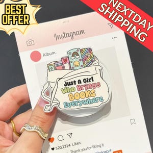 May include: A white and colorful phone grip featuring a cartoon illustration of a bag filled with books. The text on the bag reads "Just A Girl Who Brings Books Everywhere." The background is a pink Instagram-themed graphic.