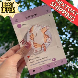 Könnte beinhalten: Ein klarer Aufkleber mit einer Cartoon-Katze mit orangefarbenem Tabby-Muster in einer verspielten Pose, vor einem lilafarbenen Instagram-Hintergrund. Der Hintergrund enthält das Instagram-Logo, ein Herzsymbol und den Text "Album. Thank you for liking it". Der Aufkleber hat den Text "NNN".