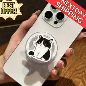 May include: A white smartphone with a black and white cat phone grip attached. The phone grip features a cartoon cat with an angry expression. The image also includes a "Best Offer" and "Next Day Shipping" banner.