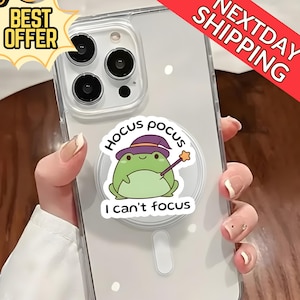 Op de afbeelding: Transparante telefoonhoes met een cartoon kikker met een heksenhoed en toverstaf. De tekst "Hocus Pocus" staat boven de kikker en "I can't focus" eronder. De hoes heeft ook stickers "Best Offer" en "Next Day Shipping".