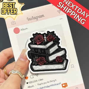 Può includere: Un adesivo raffigurante una pila di libri neri adornati con rose rosse e una candela accesa. L'adesivo è su un post di social media con il testo "Instagram" e "Album."
