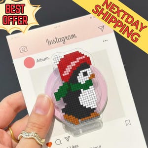 Peut inclure: Un pingouin pixélisé portant un bonnet rouge et une écharpe verte est affiché sur un fond rose sur le thème d'Instagram. Le pingouin est noir, blanc et marron. Le fond porte le mot "Instagram" et le texte "Album."