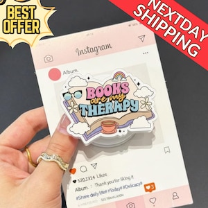 May include: A pop-up phone grip featuring the phrase "BOOKS are my THERAPY" with a book, rainbow, and coffee cup design. The grip is on a pink Instagram-themed background with a "BEST OFFER" and "NEXTDAY SHIPPING" banner.