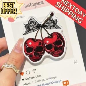 May include: A clear acrylic charm featuring two red cherries with skull faces, a black lace bow, and green stems. The charm is on a white background with Instagram-style graphics and the text "BEST OFFER" and "NEXTDAY SHIPPING".