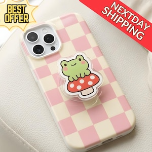 Może przedstawiać: Etui na telefon z różowo-białym wzorem w kratę. Zielona żaba siedzi na czerwonym grzybku z uchwytem popsocket. Widoczne są napisy "BEST OFFER" i "NEXTDAY SHIPPING".