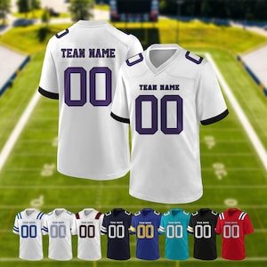May include: White football jersey with purple numbers and the text "TEAN NAME". The jersey has black accents on the sleeves and shoulders. Below are several jerseys in different colors, including blue, black, and red.
