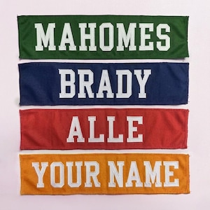 May include: Four rectangular fabric banners in green, navy blue, red, and orange. Each banner has white embroidered text: "MAHOMES", "BRADY", "ALLE", and "YOUR NAME". The banners are likely for sports fans.