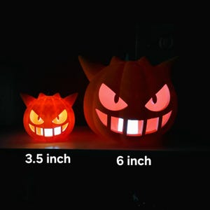 Puede incluir: Dos figuras de Gengar de color naranja, brillantes y con forma de calabaza, con orejas puntiagudas y sonrisas anchas. La figura más pequeña está marcada como 3.5 pulgadas y la más grande como 6 pulgadas. Ambas emiten luz brillante.