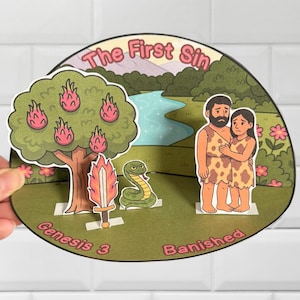 Puede incluir: Un diorama de papel que representa una escena del Génesis 3, con el texto "The First Sin" y "Genesis 3 Banished". La escena incluye un árbol con fruta rosa, una serpiente, una espada y dos figuras.