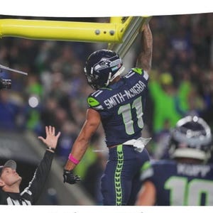 May include: A tapestry featuring a football game scene. A player in a blue and green uniform with the name "SMITH-NJIGBA" and the number "11" is reaching for the ball near a yellow goalpost. A referee is signaling with arms raised.