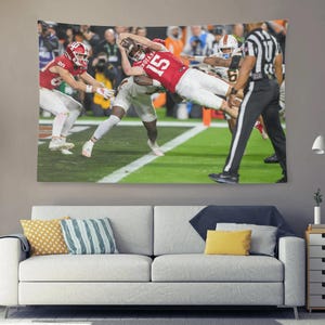 May include: A large wall tapestry depicting a football game in action. The image shows players in red and white uniforms, with the number 15 visible on one player's jersey. A referee in black and white stripes is also present.