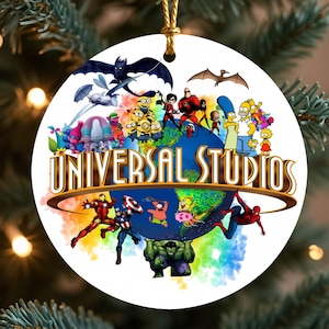 May include: A white, round Christmas ornament featuring a colorful design with characters from Universal Studios movies and shows. The ornament has a gold string for hanging and the words "UNIVERSAL STUDIOS" in gold.