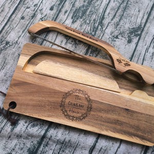 May include: A wooden bread board and a matching wooden bread knife with a metal blade. The board features a circular engraving that reads The Colin & Amy House. The knife handle is engraved with Warm Bread, Warm Hearts and Colin & Amy.