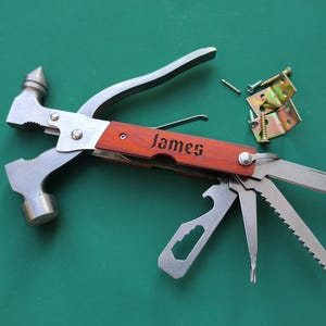 Può includere: Un multiutensile con martello, coltello e altri strumenti. L'impugnatura è color legno con il nome "James" inciso. È visibile hardware aggiuntivo, tra cui viti e cerniere. Gli strumenti sono in metallo.