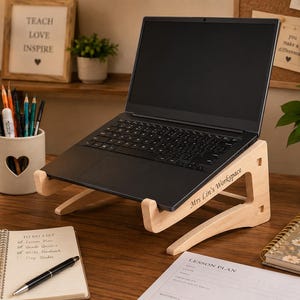 May include: A light-coloured wooden laptop stand with a smooth finish, featuring the engraved text "Mrs Lin's Workspace" on the side panel. The stand is designed with two curved support legs and a front ledge to hold a black laptop at an angle.