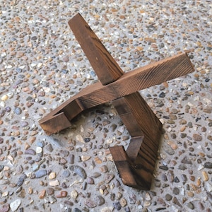 May include: A handcrafted wooden wine bottle holder. The holder is made of dark brown wood and has a unique, angular design. The holder is designed to cradle a wine bottle. The wood grain is visible.