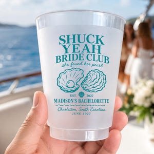 May include: A frosted plastic cup featuring teal text that reads SHUCK YEAH BRIDE CLUB, she found her pearl, EST. 2027, MADISON'S BACHELORETTE, Charleston, South Carolina, JUNE 2027, with a graphic illustration of an open oyster shell with a pearl.