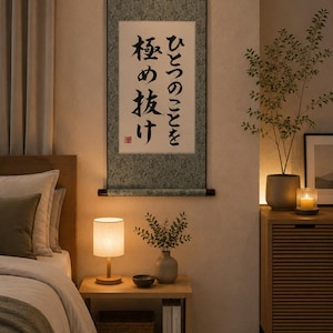 May include: A vertical wall hanging scroll featuring a sage green patterned border and a white central panel with black Japanese calligraphy text that reads ひとつのことを極め抜け, finished with a dark wooden rod at the top and bottom.