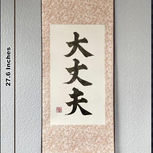 以下が含まれることがあります： 黒いインクで書かれた3つの縦書きの漢字が特徴の、長さ70cm、幅34cmの日本の書道巻物。巻物には、花柄のクリーム色の背景と、下部に濃い茶色の木の棒があります。