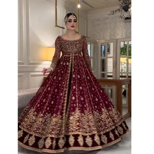 May include: A burgundy formal gown with intricate gold embroidery. The long-sleeved dress features a detailed bodice and a flowing skirt, suitable for special occasions. The gown is adorned with delicate embellishments and a matching headpiece.