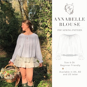 Può includere: Una camicetta azzurra con maniche lunghe e una gonna a balze. L'immagine mostra anche un cesto di fiori e il testo "ANNABELLE BLOUSE PDF SEWING PATTERN". Il modello è disponibile nelle taglie 6-26 ed è adatto ai principianti.