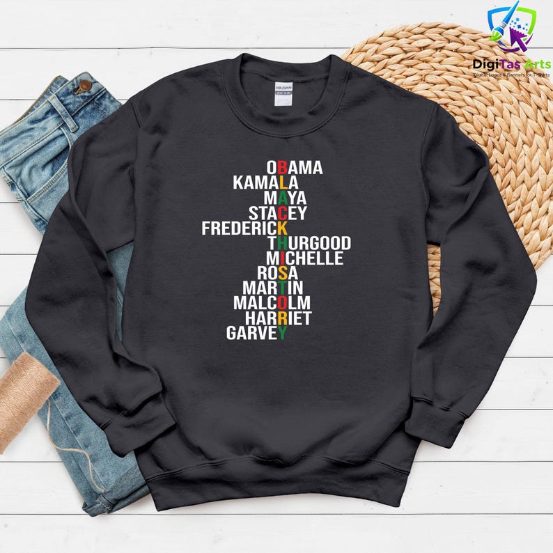 May include: A dark grey sweatshirt displaying a list of names in white, with some names highlighted in red, green, and yellow. The names include Obama, Kamala, Maya, Stacey, Frederick, Thurgood, Michelle, Rosa, Martin, Malcolm, Harriet, and Garvey.