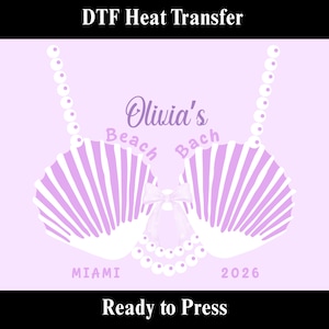 May include: A light purple DTF heat transfer design featuring a seashell bra with the text "Olivia's Beach Bach Miami 2026". The design includes a bow and pearl accents, with the words "Ready to Press" at the bottom.