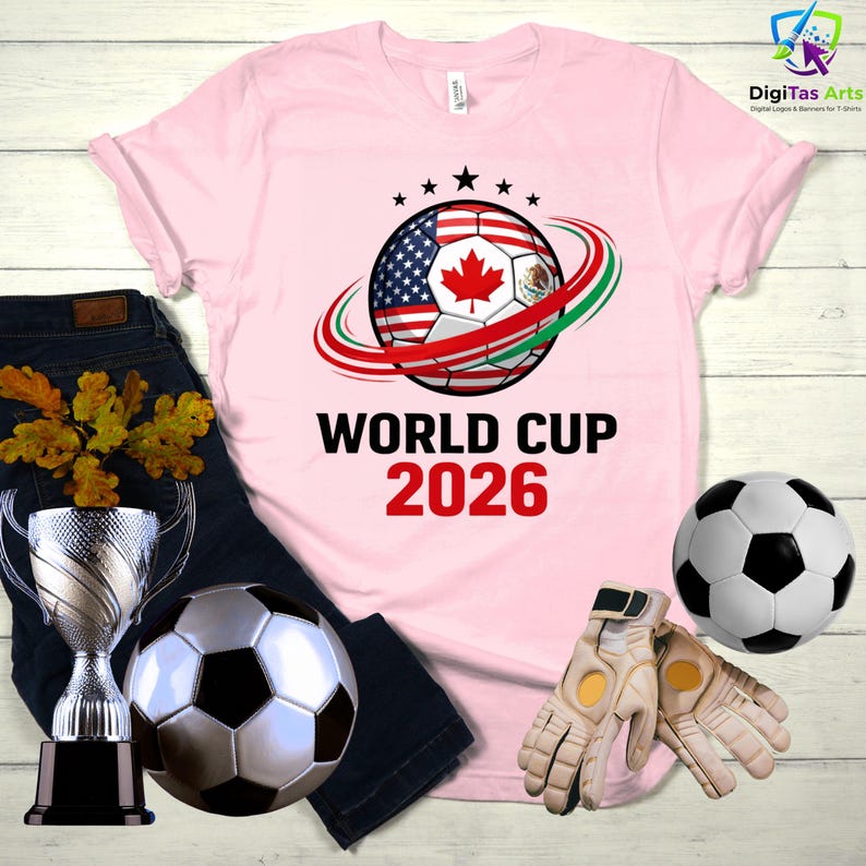 Może przedstawiać: Jasnor&oacute;żowa koszulka z nadrukiem piłki nożnej z flagami Stan&oacute;w Zjednoczonych, Kanady i Meksyku. Tekst "WORLD CUP 2026" jest wydrukowany poniżej. Dodatkowo piłka nożna, trofeum i rękawice.