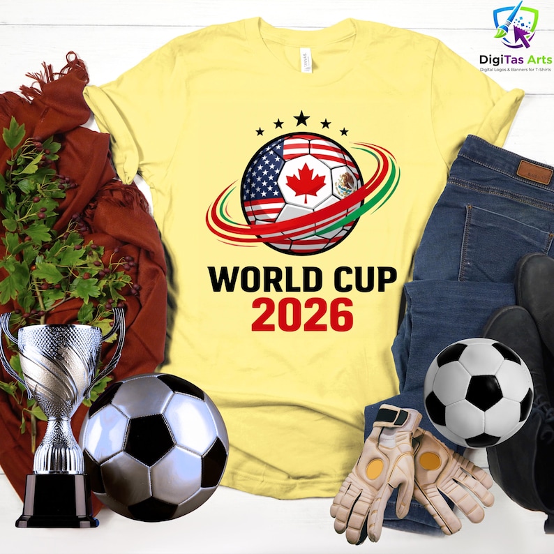 Może przedstawiać: Ż&oacute;łta koszulka z motywem piłki nożnej z flagami Stan&oacute;w Zjednoczonych, Kanady i Meksyku, z napisem "WORLD CUP 2026". Obraz zawiera piłkę nożną, rękawice, trofeum i dżinsy.