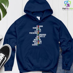 May include: A navy blue hoodie featuring the names "OBAMA, KAMALA, MAYA, STACEY, FREDERICK, THURGOOD, MICHELLE, ROSA, MARTIN, MALCOLM, HARRIET, GARVEY" printed vertically in different colours. The hoodie has a drawstring hood.