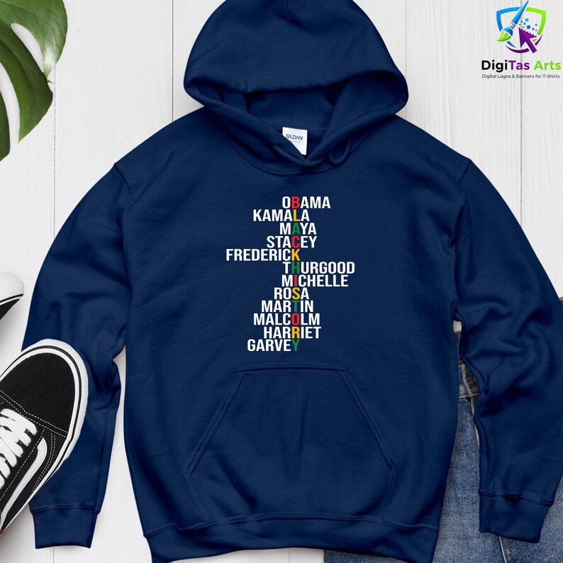 May include: A navy blue hoodie featuring the names "OBAMA, KAMALA, MAYA, STACEY, FREDERICK, THURGOOD, MICHELLE, ROSA, MARTIN, MALCOLM, HARRIET, GARVEY" printed vertically in different colours. The hoodie has a drawstring hood.