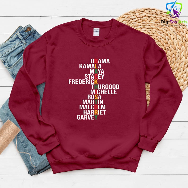 May include: A maroon sweatshirt featuring the names Obama, Kamala, Maya, Stacey, Frederick, Thurgood, Michelle, Rosa, Martin, Malcolm, Harriet, and Garvey in white, red, yellow, and green text.