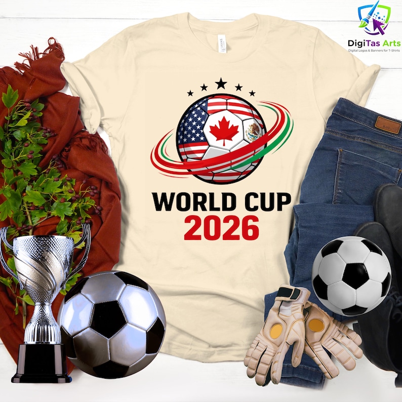 Może przedstawiać: Kremowa koszulka z motywem piłki nożnej z flagami USA, Kanady i Meksyku, z napisem "WORLD CUP 2026". Zawiera piłkę nożną, rękawice, trofeum i parę dżins&oacute;w.