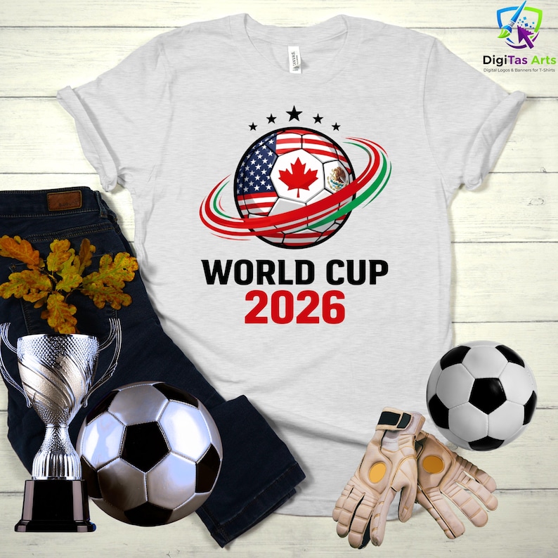 Może przedstawiać: Biała koszulka z nadrukiem piłki nożnej z flagami Stan&oacute;w Zjednoczonych, Kanady i Meksyku. Tekst "WORLD CUP 2026" jest wydrukowany poniżej w kolorze czarnym i czerwonym. Dodatkowo piłka nożna, trofeum i rękawice bramkarskie.
