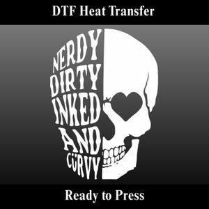 Peut inclure: Un motif de crâne blanc avec une orbite en forme de cœur et les mots "Nerdy Dirty Inked And Curvy" dans une police stylisée. Le texte "DTF Heat Transfer" et "Ready to Press" sont également inclus. Le motif est sur fond gris foncé.