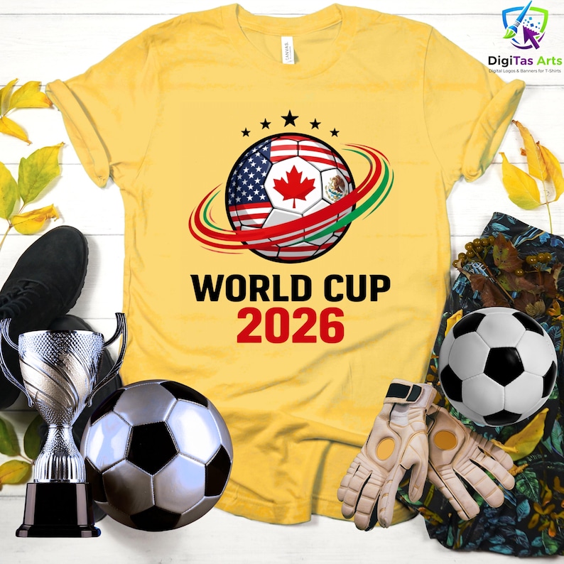 Może przedstawiać: Ż&oacute;łta koszulka z motywem piłki nożnej z flagami USA, Kanady i Meksyku, z napisem "WORLD CUP 2026". Zawiera piłki nożne, rękawice i trofeum.