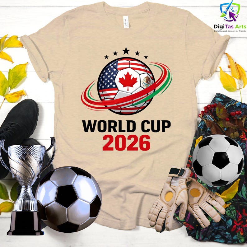 Może przedstawiać: Beżowa koszulka z motywem piłki nożnej z flagami USA, Kanady i Meksyku, z napisem "WORLD CUP 2026". Zawiera piłkę nożną, trofeum i rękawice.