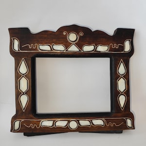 May include: A rectangular dark brown wooden picture frame featuring inlaid white shell accents in geometric shapes including circles, triangles, and teardrops. The frame has a decorative scalloped top edge and a smooth, polished finish throughout.