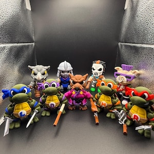 May include: A collection of Teenage Mutant Ninja Turtles figurines, each with distinct colored masks and weapons. The figures include Leonardo, Donatello, Raphael, and Michelangelo, along with other characters. The figures are green, brown, and various other colors.