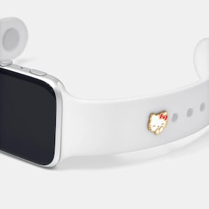 May include: A white smartwatch with a silver case and a white silicone band. The band features a gold-colored Hello Kitty charm with a red bow. The watch is designed for everyday wear and is a stylish accessory.